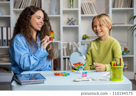 Cute long-haired speech therapist working with a blonde boy, both smiling Cute long-haired speech therapist working with a blonde boy, both smiling 118194575