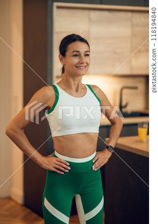Charming young woman in sportswear standing in home kitchen after doing workout Charming young woman in sportswear standing in home kitchen after doing workout 118194840