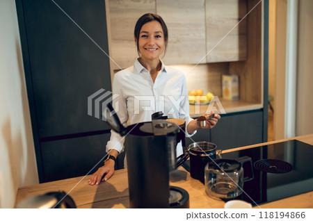 Dark-haired young woman in the kitchen making coffee in the coffee machine Dark-haired young woman in the kitchen making coffee in the coffee machine 118194866