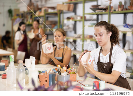 Young man sits near table and decorates clay ceramic craft vase, plate Young man sits near table and decorates clay ceramic craft vase, plate 118196975