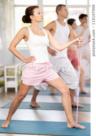 Happy young active woman with group people in sportswear, standing and training exercise with resistance bands in gym Happy young active woman with group people in sportswear, standing and training exercise with resistance bands in gym 118197006