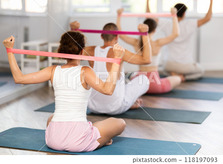 Young woman doing shoulder workout with resistance band sitting cross-legged Young woman doing shoulder workout with resistance band sitting cross-legged 118197093