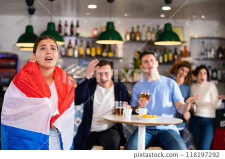 Young upset female wrapping herself in Dutch flag and supporting national team in pub 118197292