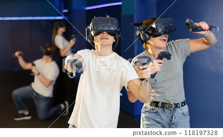 Emotional young couple with VR headsets and joysticks immersed in game Emotional young couple with VR headsets and joysticks immersed in game 118197328