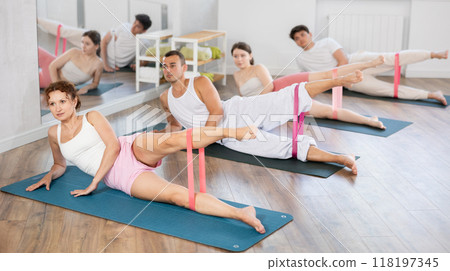 Young men and women practicing leg lift with band on knees lying on the side Young men and women practicing leg lift with band on knees lying on the side 118197345