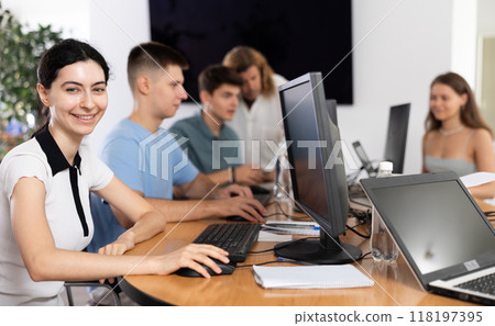 Positive interested young girl using computer in busy library 118197395