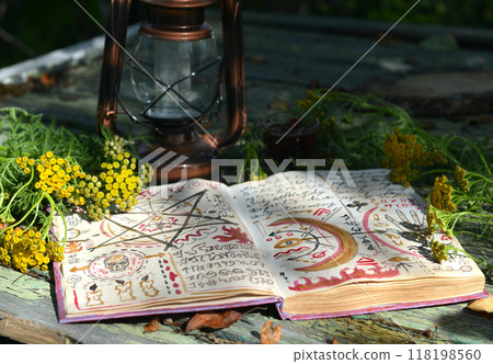 Mystic still life with magic book of spells, old lantern and healing herbs on old table. Occult, esoteric, wicca and divination concept. No foreign language, all symbols are fictional Mystic still life with magic book of spells, old lantern and healing herbs on old table. Occult, esoteric, wicca and divination concept. No foreign language, all symbols are fictional 118198560