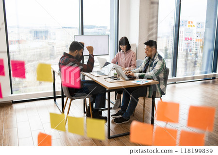 Architects brainstorming in modern office with sticky notes on glass Architects brainstorming in modern office with sticky notes on glass 118199839