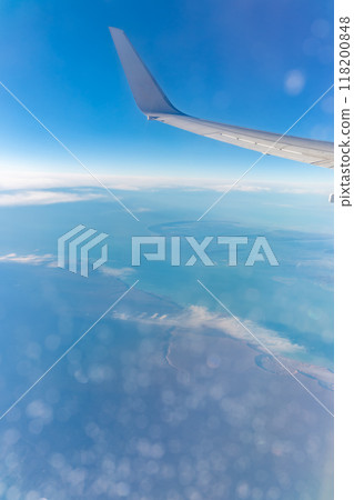 View from the airplane window at a beautiful blue clear sky, earth, sea and the airplane wing View from the airplane window at a beautiful blue clear sky, earth, sea and the airplane wing 118200848