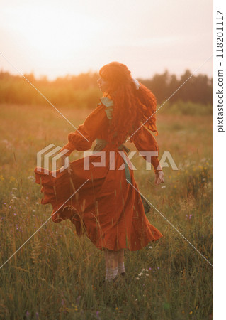 A shepherdess woman with red hair and a green dress sits in a field of flowers. Rear view. A shepherdess woman with red hair and a green dress sits in a field of flowers. Rear view. 118201117