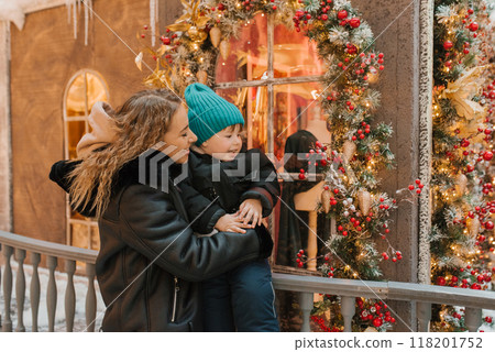 Mother and child are standing outside a store with a Christmas tree in the window. They both seem to be enjoying the festive atmosphere Mother and child are standing outside a store with a Christmas tree in the window. They both seem to be enjoying the festive atmosphere 118201752