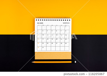 Top view of March 2025 desk calendar and pencil on yellow and black background. 118205867