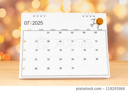 July 2025 desk calendar on wooden table with gold light bokeh background. 118205868