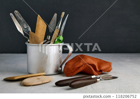 Many stacks and sculpting tools in a metal mug and pieces of clay and plasticine on a concrete table in a sculptor's workshop 118206752