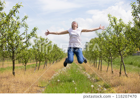 An adult woman rejoices and jumps up against the backdrop of a blooming spring garden. 118207470