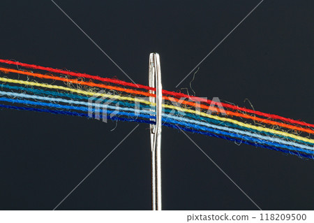 multi-colored threads for sewing in the form of a rainbow pass through an antique needle on a black background 118209500