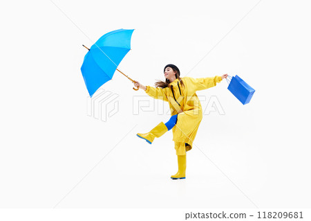 Cheerful woman in vibrant raincoat leaps with blue shopping bag and umbrella, embracing rainy weather against white background. Cheerful woman in vibrant raincoat leaps with blue shopping bag and umbrella, embracing rainy weather against white background. 118209681