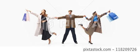 Banner. Man stands in shock while women holding shopping bags and reaching to distance against white studio background. Banner. Man stands in shock while women holding shopping bags and reaching to distance against white studio background. 118209726