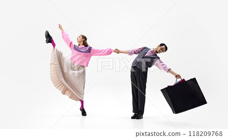Woman kicks high while holding her partner's hand. Both carry shopping bags against white studio background. 118209768