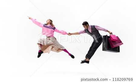 Dynamic photo of playful couple jumps hand in hand, holding shopping bags against white studio background. 118209769