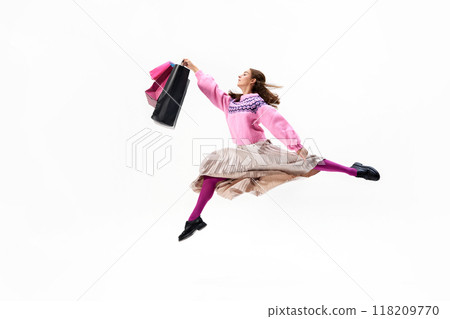Leaping through air with bags in hand, young woman showcases her bright and vibrant stylish outfit against white studio background. 118209770