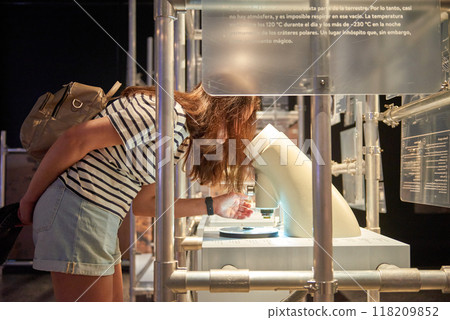 Young Scientist in Action: Girl Engrossed in Microscope Exploration at Interactive Museum Science Exhibit. Educational Adventure: Enthusiastic Girl Discovering Microscopic Wonders in Museum's Science Young Scientist in Action: Girl Engrossed in Microscope Exploration at Interactive Museum Science Exhibit. Educational Adventure: Enthusiastic Girl Discovering Microscopic Wonders in Museum's Science 118209852