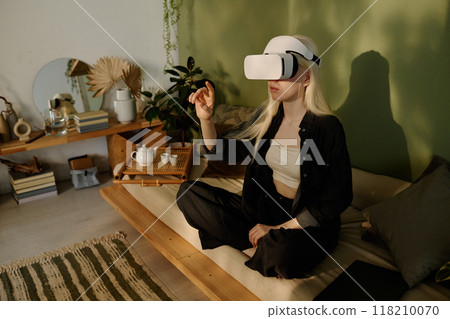 High angle of young woman with albinism wearing headset sitting on couch with legs crossed using virtual reality app High angle of young woman with albinism wearing headset sitting on couch with legs crossed using virtual reality app 118210070