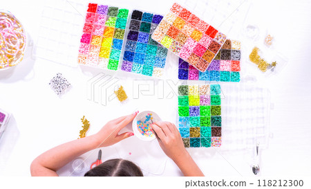 Flat lay. Delicate fingers of a young girl navigate through a treasure trove of bright, multicolored beads, each compartment revealing a new hue to choose from. 118212300