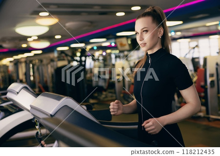 Young woman jogging on a treadmill in a modern gym during morning hours 118212435
