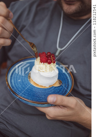 Close up of delicious tart. Close up of Caucasian man eating dessert with meringue swirl and berries in a cafe 118212541