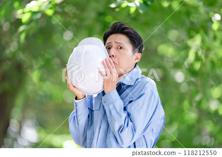 A man in work clothes hiding his face with a helmet A man in work clothes hiding his face with a helmet 118212550