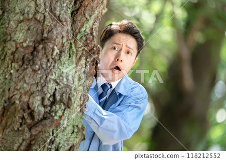 A man in work clothes hiding behind a tree 118212552