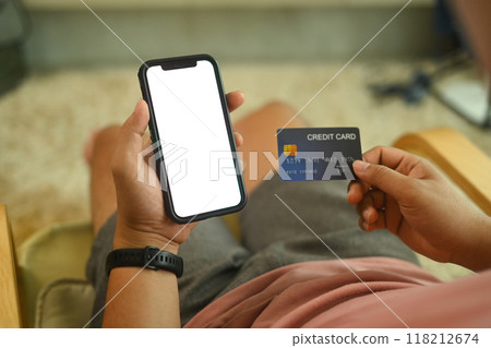 Close up shot of man holding a credit card and purchasing online on smartphone 118212674