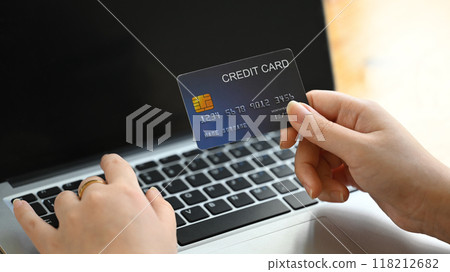 Close up of a person holding a credit card in front of a laptop, making online transaction Close up of a person holding a credit card in front of a laptop, making online transaction 118212682