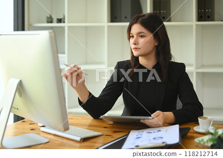 Professional businesswoman holding digital tablet and analyzing financial data on computer monitor 118212714