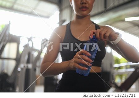 Sporty young woman drinking water while resting after exercising at health club 118212721