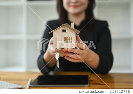 Confident female realtor holding a model house with key. Real estate appraisal and property concept 118212726