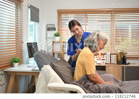 Healthcare professional in blue scrubs using a stethoscope to check breathing of an elderly female patient 118212746