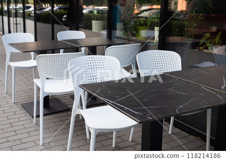 Outdoor cafe seating with white plastic chairs and black marble tables. 118214186