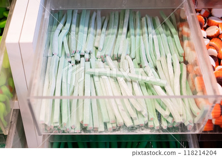 Green striped licorice candies in a transparent plastic bin. Close-up shot of candy display 118214204
