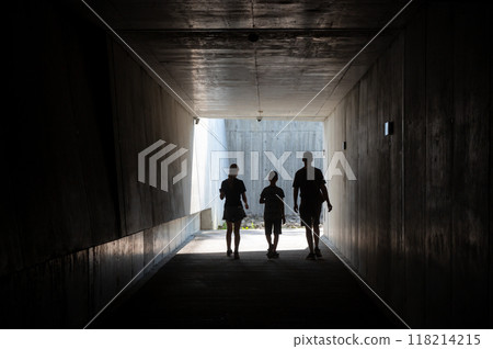 Silhouette of three people walking through a dark tunnel towards the light. Silhouette of three people walking through a dark tunnel towards the light. 118214215