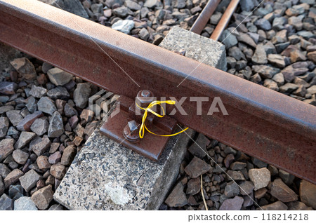 Close-up of a rusty railway track with a yellow ribbon tied around a bolt. 118214218