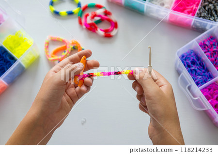 Child making colorful rubber band bracelet with a loom tool Child making colorful rubber band bracelet with a loom tool 118214233