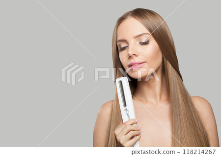 Smiling woman with hair straightener iron in studio isolated on white background. Smiling woman with hair straightener iron in studio isolated on white background. 118214267