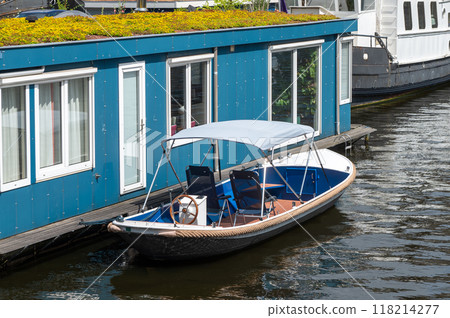Small motorboat moored next to a blue floating house on a canal. 118214277