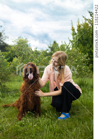 Attractive young woman with Irish setter dog outdoors. Woman on a green grass with dog Attractive young woman with Irish setter dog outdoors. Woman on a green grass with dog 118214422