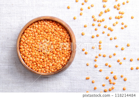 Red lentils in a wooden bowl on linen. Lentil variety with husk removed for a shorter cooking time and no soaking needed. Dried fruits of Lens culinaris, an edible legume with lens-shaped seeds. 118214484