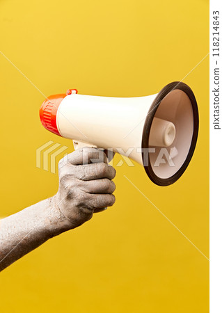 Zombie-like hand holding megaphone against yellow background. News, sales, announcement Zombie-like hand holding megaphone against yellow background. News, sales, announcement 118214843