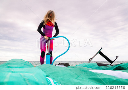 Young sportswoman in a wetsuit pumps her kite on the beach in cloudy weather Young sportswoman in a wetsuit pumps her kite on the beach in cloudy weather 118215358