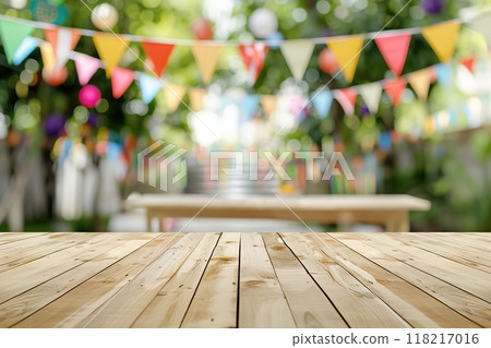 Wooden table desk surface for product display on a blurred festive background with colorful flags, park green leaves bokeh. Outdoor decorated for a festive celebration, garden picnic. Party banner 118217016